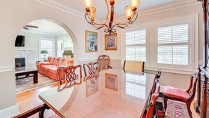 Un salon spacieux avec une grande table à manger, d’élégantes chaises en bois, un lustre et une cheminée.