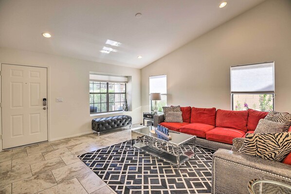A spacious living room with a red sofa, a patterned rug, and a glass coffee table.