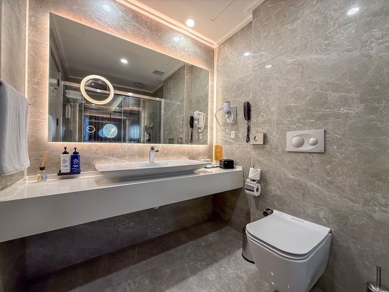 A modern bathroom with a large mirror, a sink, a toilet, and a shower area.