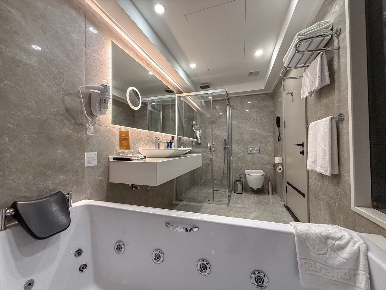 A modern bathroom with a large bathtub, a glass-enclosed shower, a vanity with a mirror, and a towel rack.