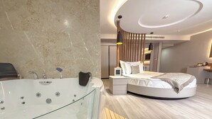 Un dormitorio moderno con un jacuzzi con paredes de vidrio, una cama curvada y piso de madera.