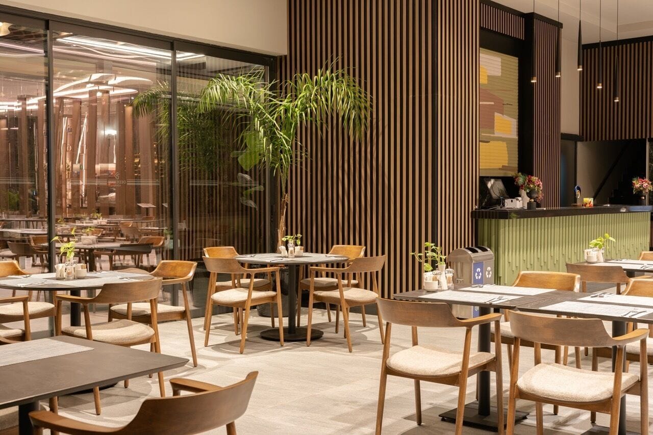 A modern restaurant with wooden furniture, a large plant, and a glass wall.