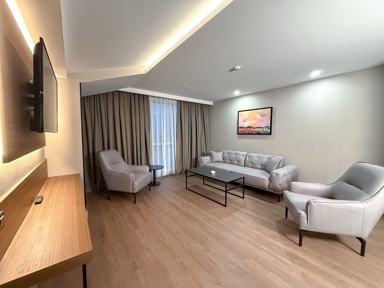Un salon moderne comprenant un canapé, deux fauteuils, une table basse et un téléviseur fixé au mur.