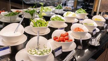 Un bufé con diversos platos, como ensaladas, verduras y un parfait de yogur.