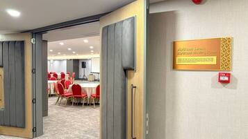 Una sala de reuniones con una puerta de madera, un letrero que la identifica como sala de reuniones y un botón rojo de emergencia en la pared.