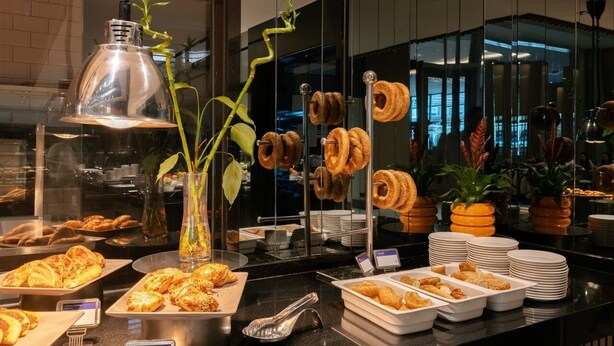 Zona de bufé con diversos alimentos, incluyendo pasteles y pan, dispuestos en fuentes y platos.
