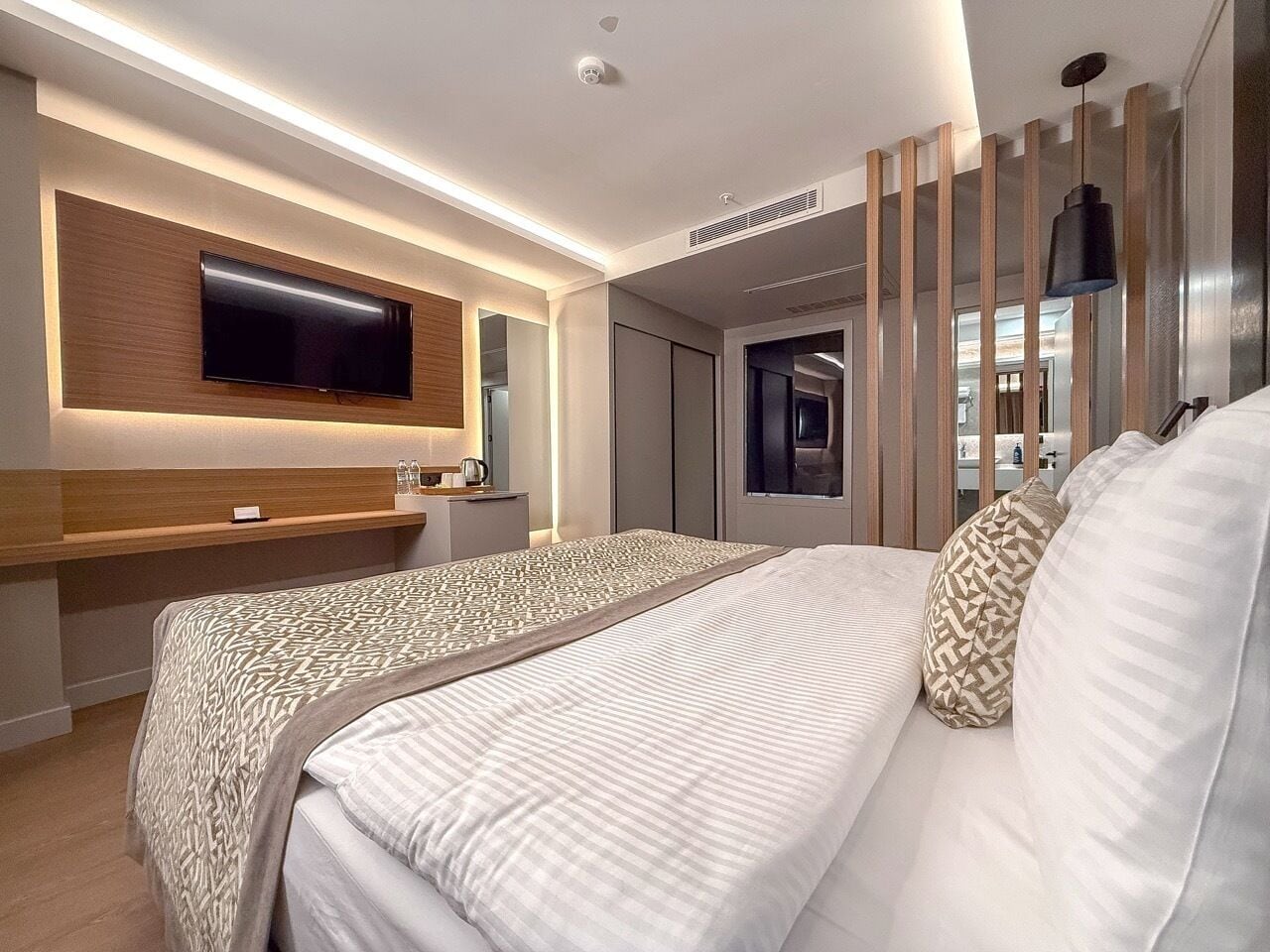 A modern hotel room with a large bed, a TV mounted on the wall, and a desk with a chair.