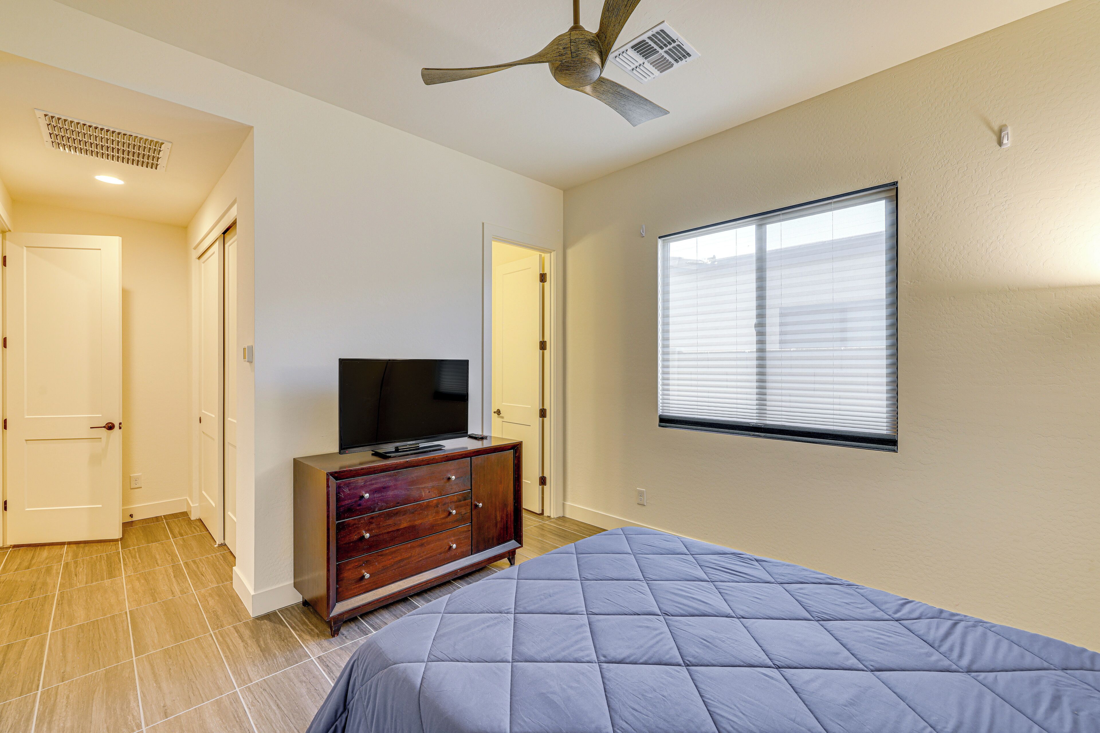 A bedroom with a bed, a dresser, a television, and a ceiling fan.