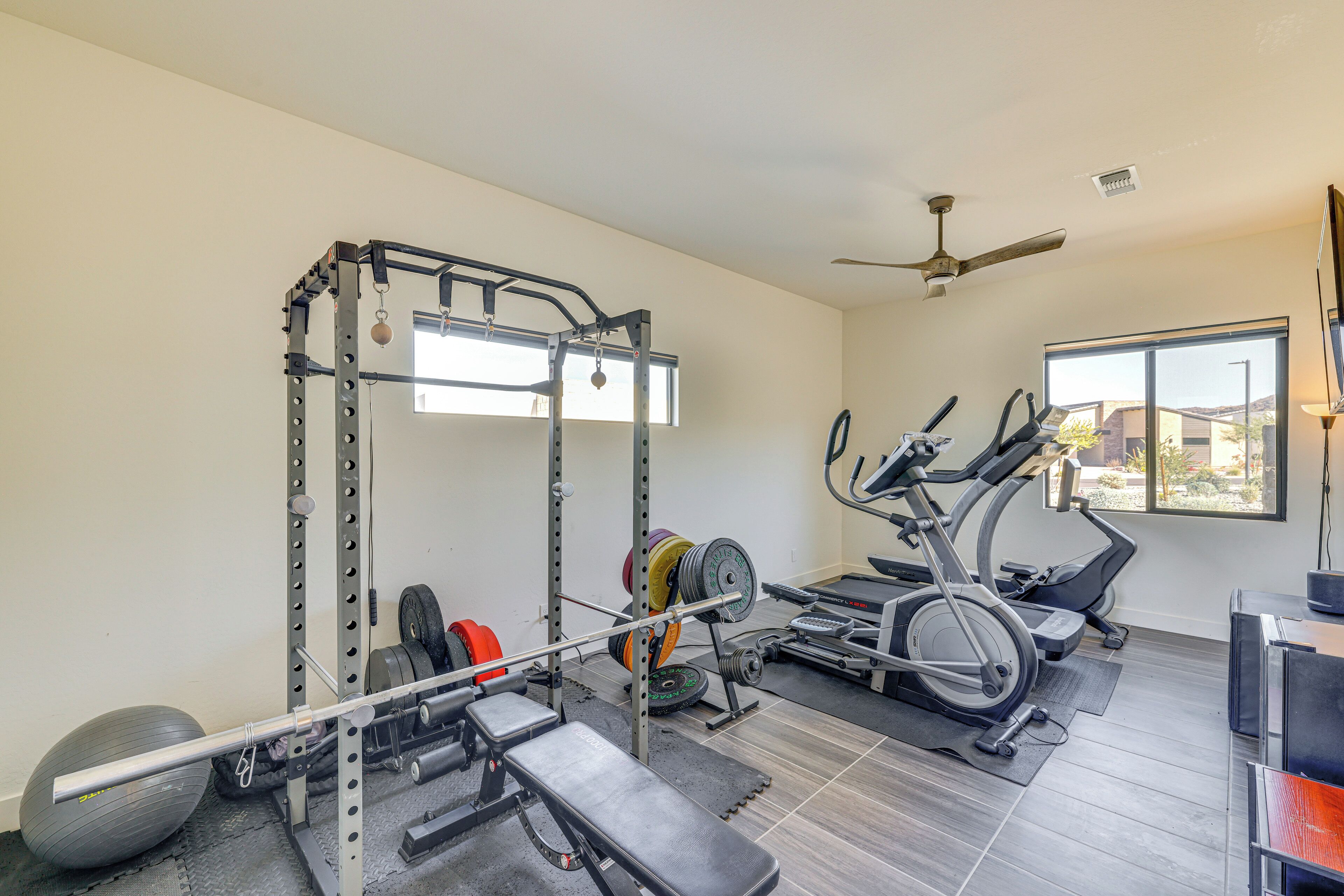 Un gimnasio en casa con una jaula para sentadillas, banco de pesas, discos de pesas, una elíptica y una bicicleta estática.