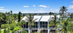 A building with a white exterior and large windows, surrounded by palm trees and a body of water in the background. - Waterfront Matlacha Condo w/ Patio & Pool Access (Matlacha)