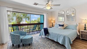 A bedroom with a bed, a chair, a balcony with a view, and a ceiling fan. - Waterfront Matlacha Condo w/ Patio & Pool Access (Matlacha)