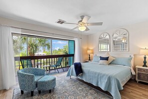 A bedroom with a bed, a chair, a balcony with a view, and a ceiling fan. - Waterfront Matlacha Condo w/ Patio & Pool Access (Matlacha)