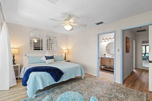 A bedroom with a bed, two bedside tables, a ceiling fan, a large window with a view, and a bathroom with a mirror and sink. - Waterfront Matlacha Condo w/ Patio & Pool Access (Matlacha)