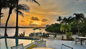 A poolside area with a view of the sunset over water, surrounded by palm trees and deck chairs. - Waterfront Matlacha Condo w/ Patio & Pool Access (Matlacha)