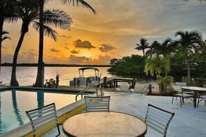 A poolside area with a view of the sunset over water, surrounded by palm trees and deck chairs. - Waterfront Matlacha Condo w/ Patio & Pool Access (Matlacha)