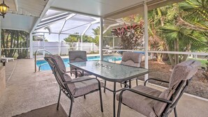 A covered outdoor area with a glass table and chairs, a pool, and tropical plants. - Tropical Cape Coral Home w/ Private Dock on Canal! (Cape Coral)