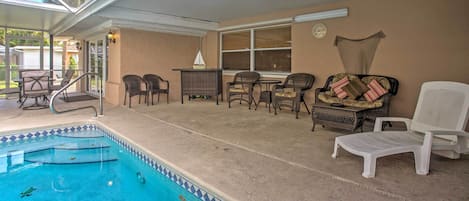 A covered outdoor swimming pool area with lounge chairs, a table, and a small sailboat model.