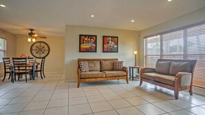 A living room with a sofa, a dining table with chairs, and two wall-mounted paintings. - Tropical Cape Coral Home w/ Private Dock on Canal! (Cape Coral)