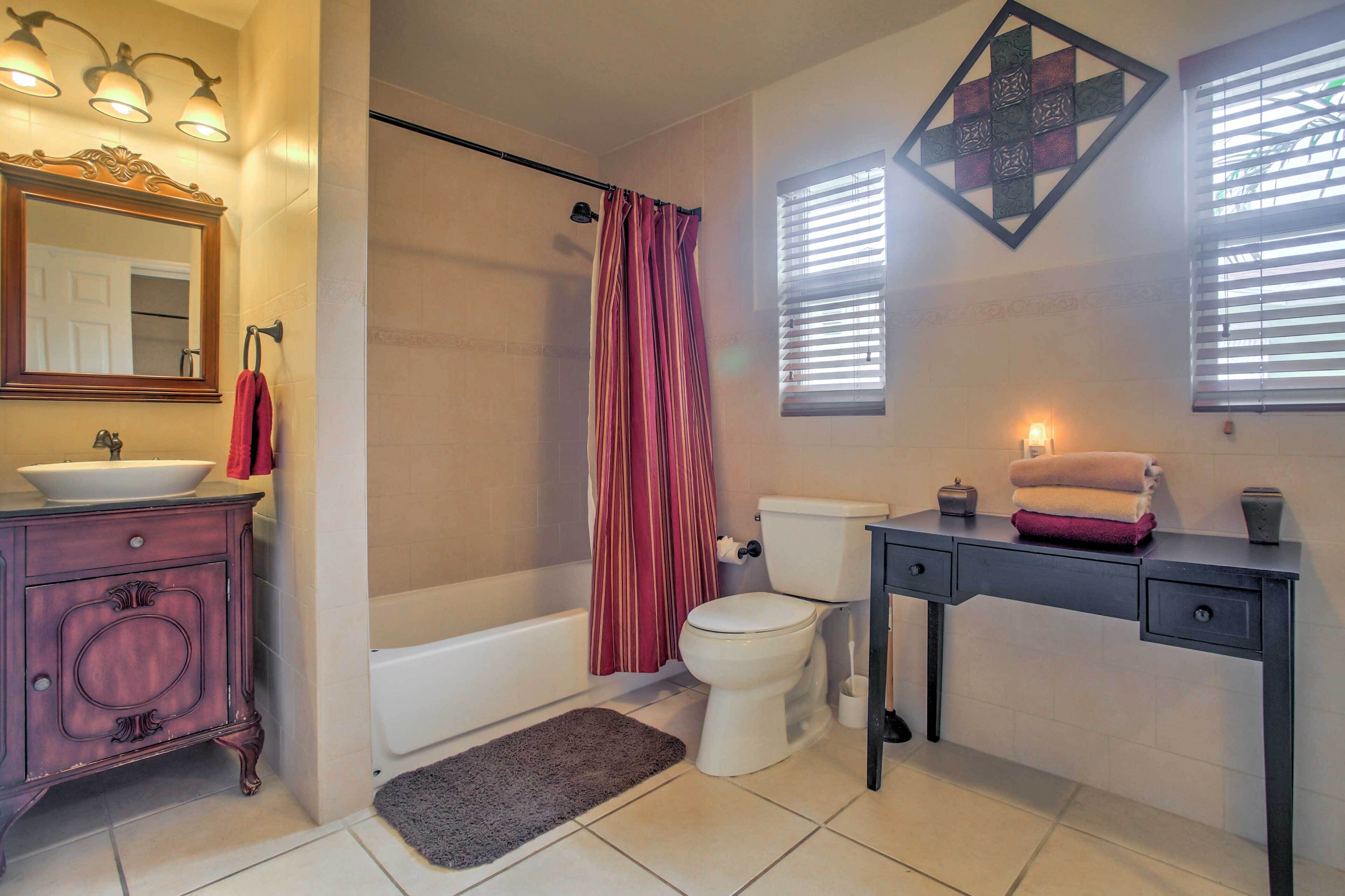 Une salle de bain comprenant un meuble-lavabo, un lavabo, un miroir, des toilettes, une baignoire, un rideau de douche et une petite table avec des serviettes.