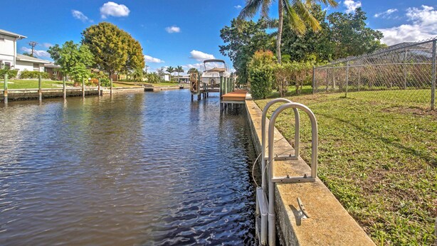 A canal with a boat dock, a grassy area, and a fence. - Tropical Cape Coral Home w/ Private Dock on Canal! (Cape Coral)