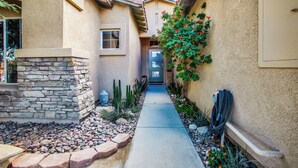 A narrow pathway leading to a house entrance, flanked by a stone wall and a variety of plants. - Near Downtown: Palm Springs Home w/ Mountain Views (Palm Springs)