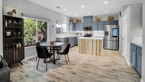 A modern kitchen with grey cabinets, stainless steel appliances, a wooden island, and a dining area with a round table and chairs. - Near Downtown: Palm Springs Home w/ Mountain Views (Palm Springs)