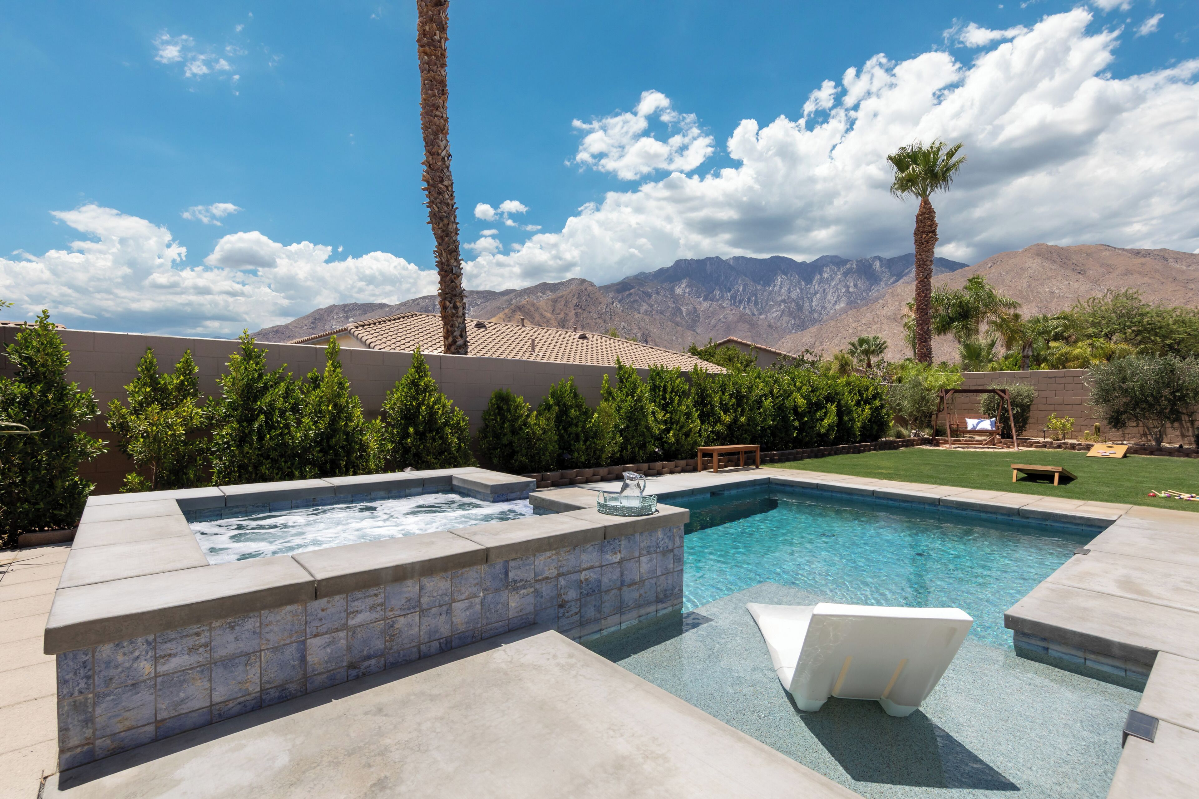 A swimming pool with a hot tub, surrounded by palm trees and a mountain backdrop.