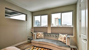 Een slaapkamer met een bank, een bed en grote ramen met uitzicht over de stad.