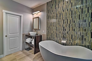 A modern bathroom with a freestanding bathtub, a vanity with a mirror, and a tiled wall with a geometric pattern. - Modern Anchorage Townhome - By Delaney Park Strip! (Anchorage)