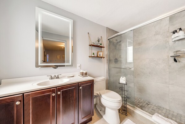 Een moderne badkamer met een grote spiegel, twee wastafels, houten kastjes, een toilet en een douchecabine met glazen wanden.