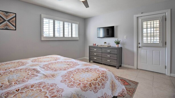 Une chambre à coucher avec un lit, un ventilateur de plafond, une commode, un téléviseur et une porte.