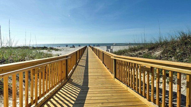 Una passerella di legno conduce a una spiaggia con dune sabbiose e un cielo sereno.
