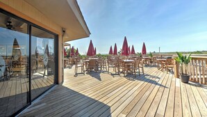 Un pontile di legno con sedute all'aperto e ombrelloni rossi, con vista su una spiaggia.
