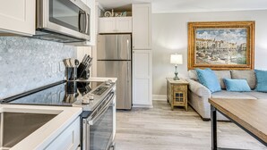Una cucina moderna con elettrodomestici in acciaio inox, una parete di fondo in marmo e una zona pranzo con tavolo in legno e divano con cuscini blu.