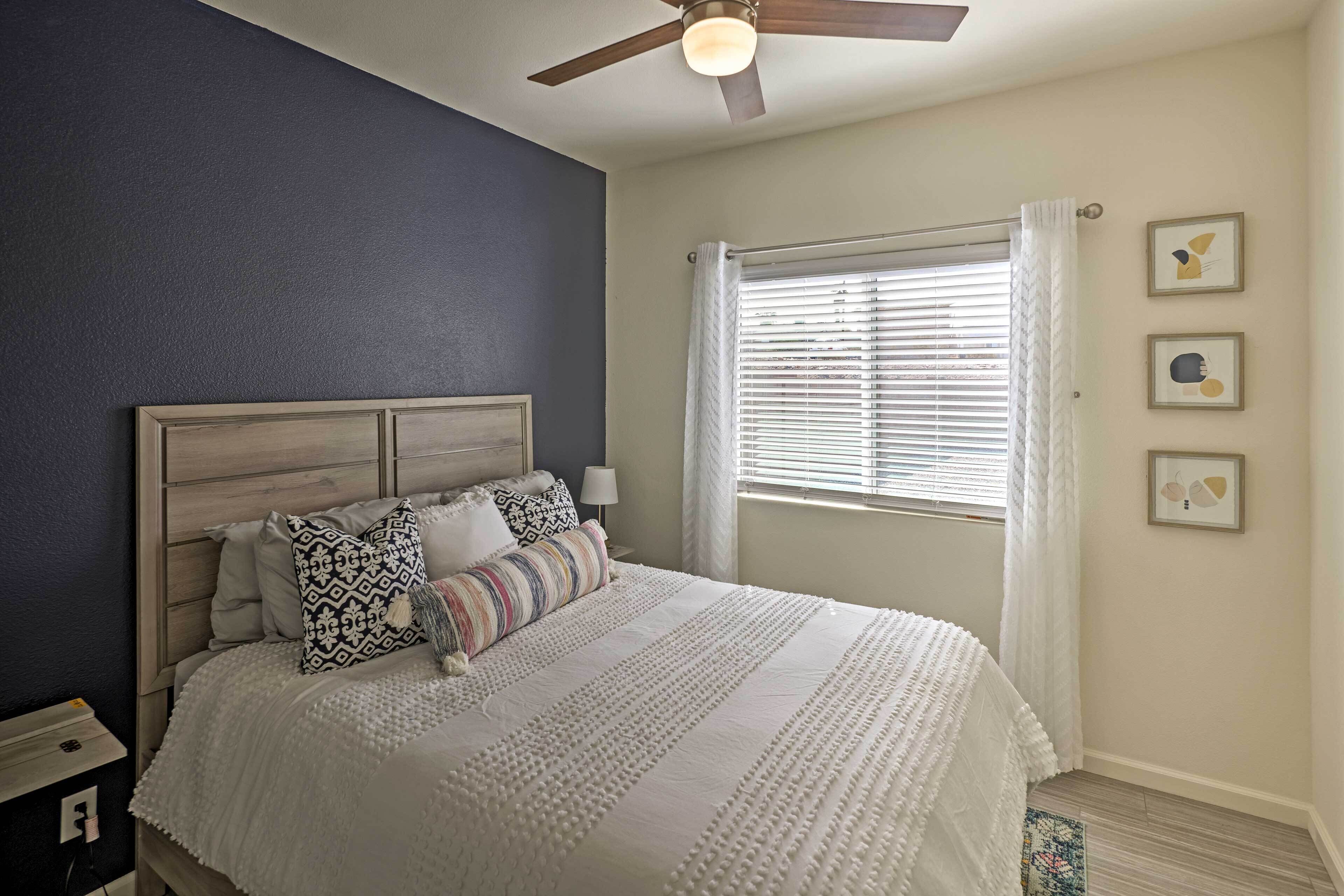 A bedroom with a bed, a ceiling fan, a window with blinds, and wall art.