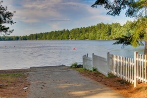 Näkymä järvelle, jossa on puinen aita, betoninen polku ja kauempana näkyvä rantaviiva, jota reunustavat puut.