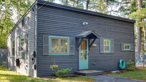 A small, single-story house with a dark gray exterior, teal trim around windows and door, and a small porch.
