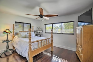 A bedroom with a wooden four-poster bed, a ceiling fan, a television on a cabinet, and a window with blinds. - Pet-friendly Oasis w/ Deck & Fire Pit in Bokeelia! (Bokeelia)