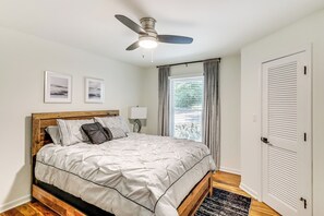 A bedroom with a wooden bed, a ceiling fan, a window with curtains, and a door with louvered panels. - Private Dock: Lake Oconee Waterfront Escape! (Eatonton)