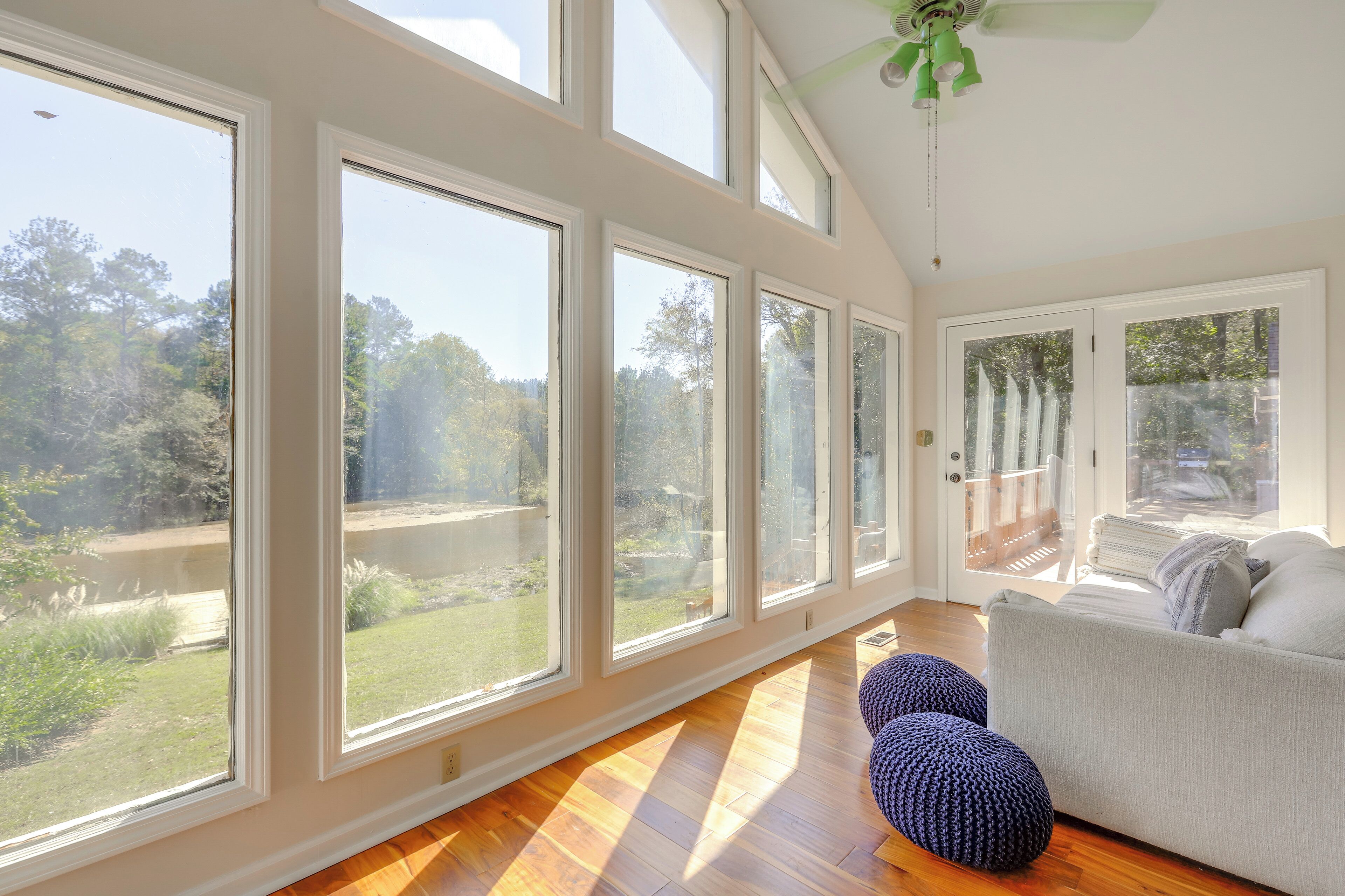 A spacious room with large windows, a ceiling fan, and a grey sofa.