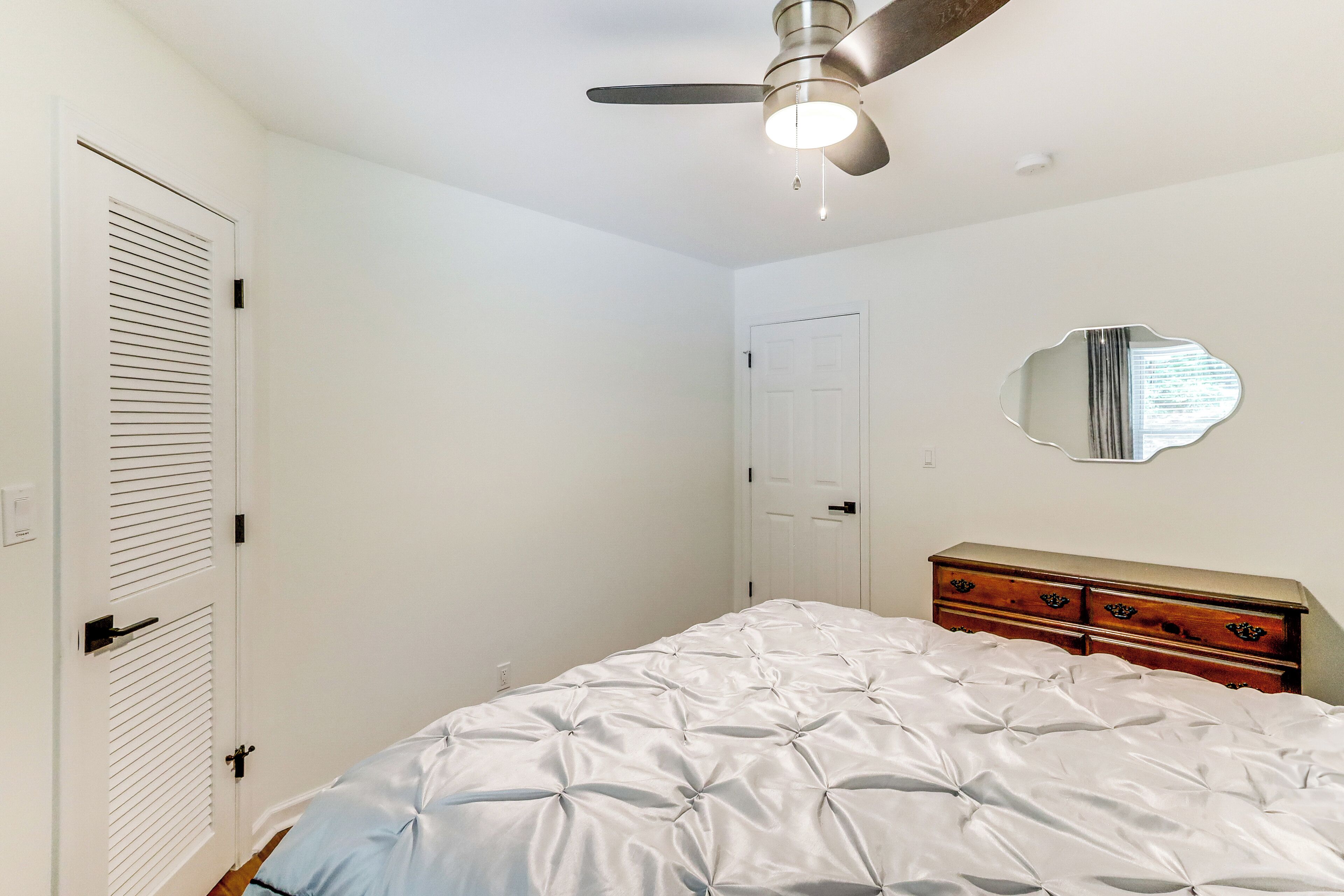 Un dormitorio con una cama, un aparador, un ventilador de techo y una puerta.