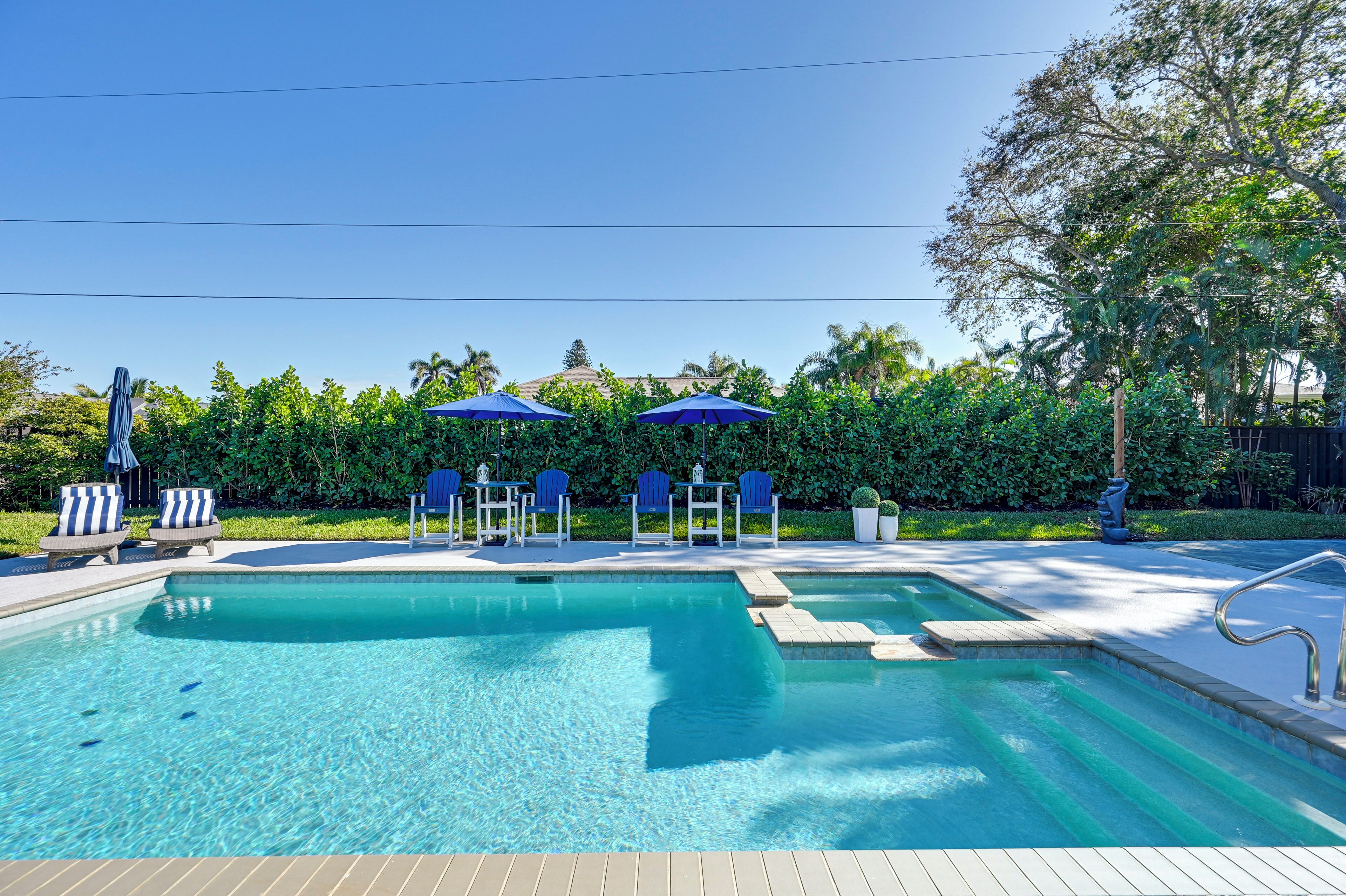 A swimming pool with blue chairs and umbrellas, surrounded by greenery.