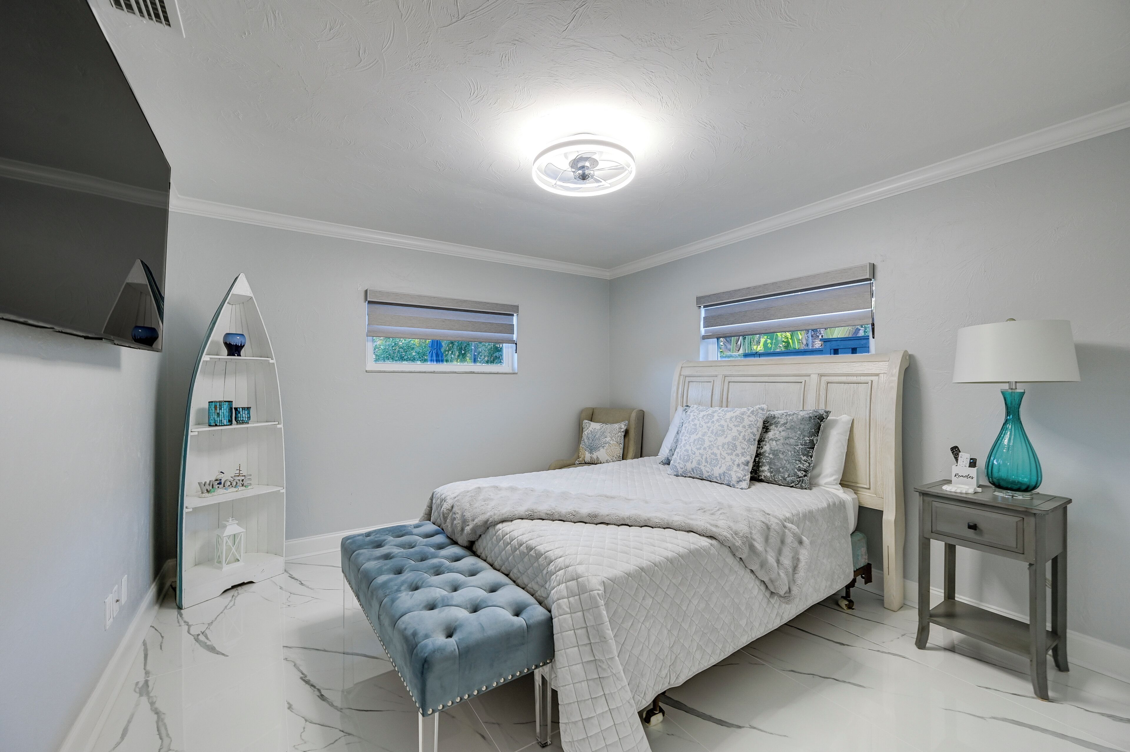 A bedroom with a bed, a bench, a nightstand, a lamp, and a shelf with decorative items.