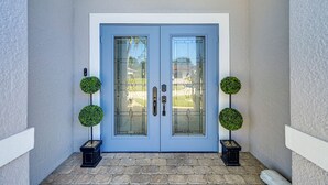 A blue double door with glass panels and two spherical topiary plants on either side. - Pool & Spa: Luxe Home in Naples! (Naples)