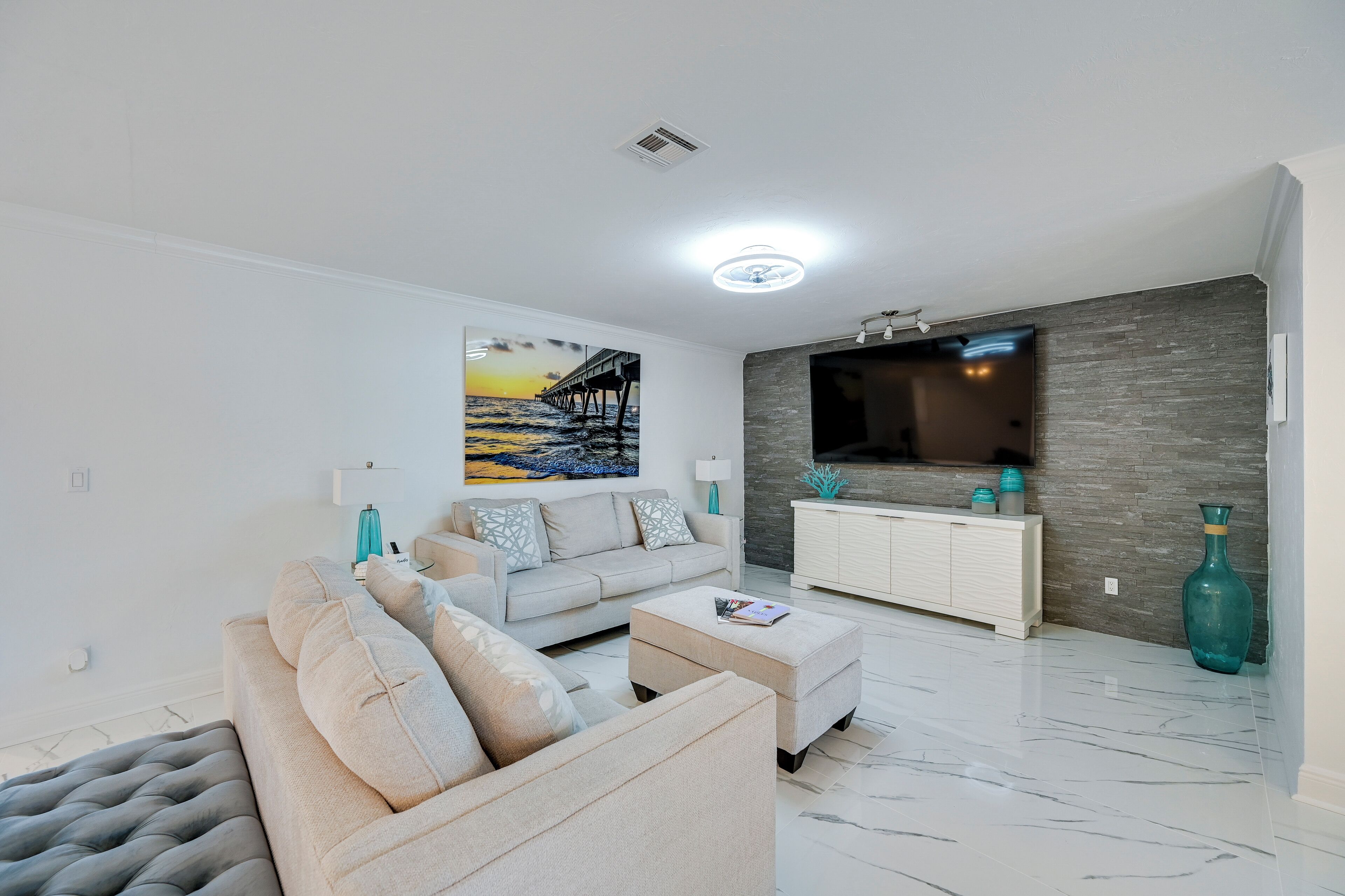 A modern living room with a grey sofa, a white coffee table, and a painting of a pier.