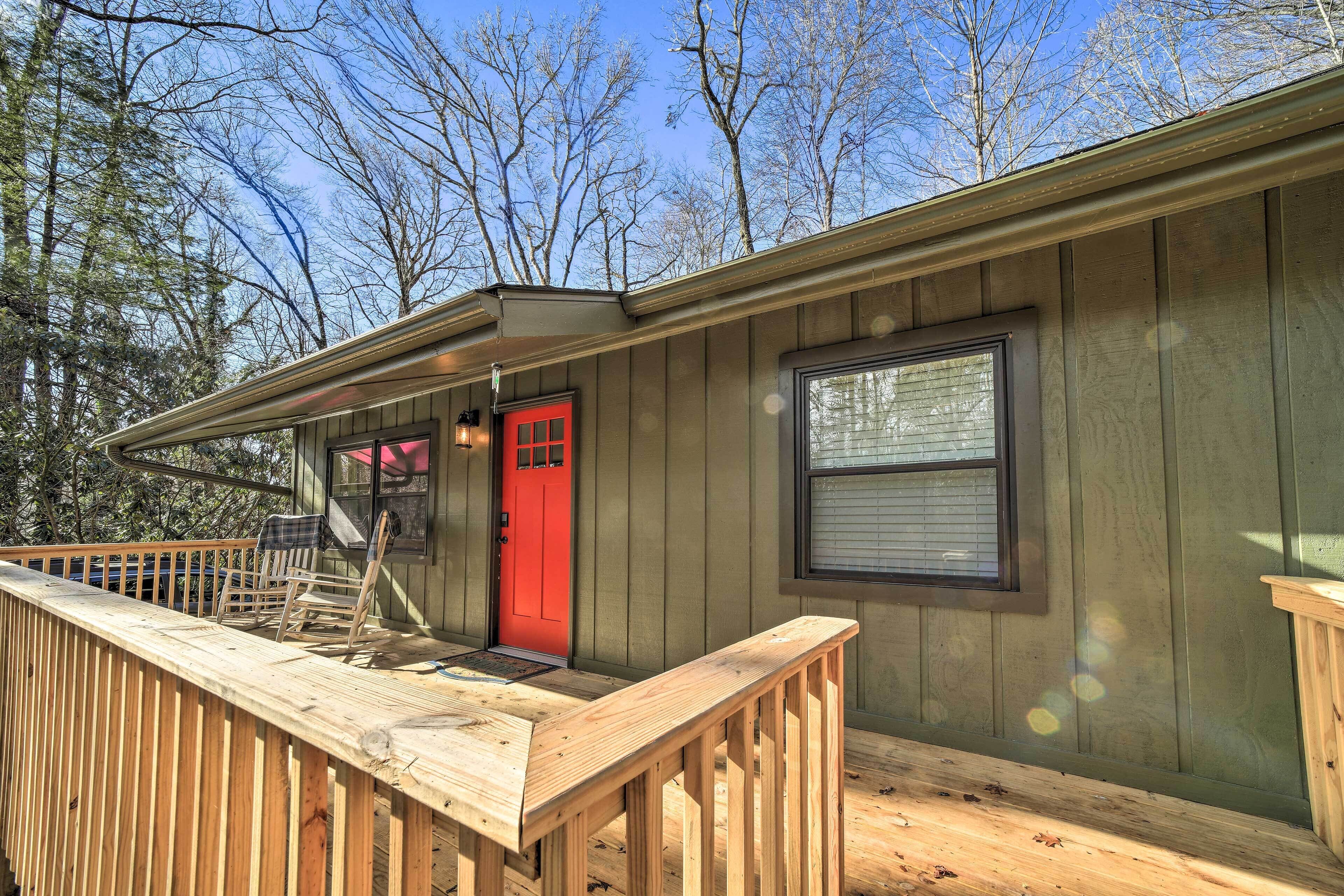 Une cabane en bois avec une porte rouge, une terrasse et une fenêtre.