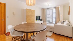 A modern living room with a round wooden dining table, white chairs, a beige sofa, and a television on a white cabinet. - Cozy Santa Cruz (Santa Cruz)