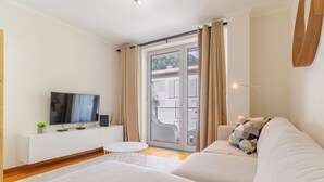 A modern living room with a sofa, a TV, a small round table, and a sliding glass door leading to an outdoor area. - Cozy Santa Cruz (Santa Cruz)