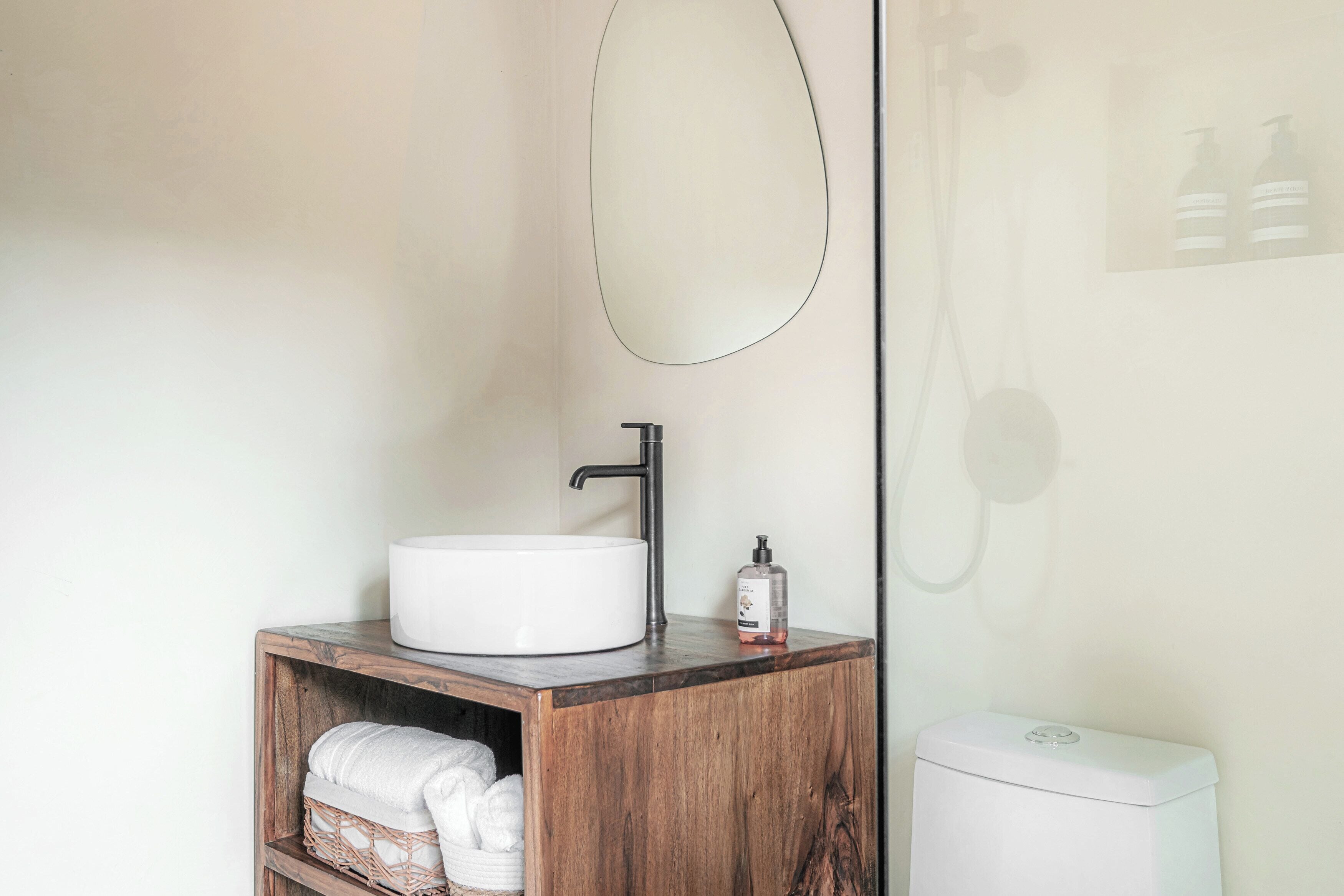 A bathroom with a white sink, a wooden vanity, a mirror, a shower, and a toilet.