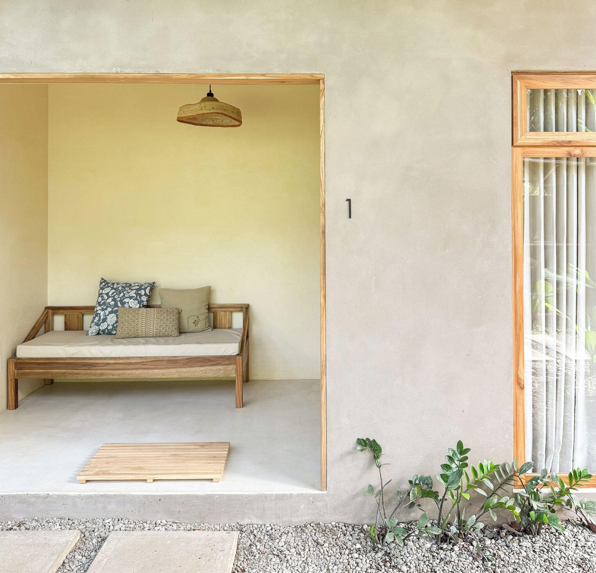 A minimalist room with a wooden bench, a hanging light fixture, and a small plant area.